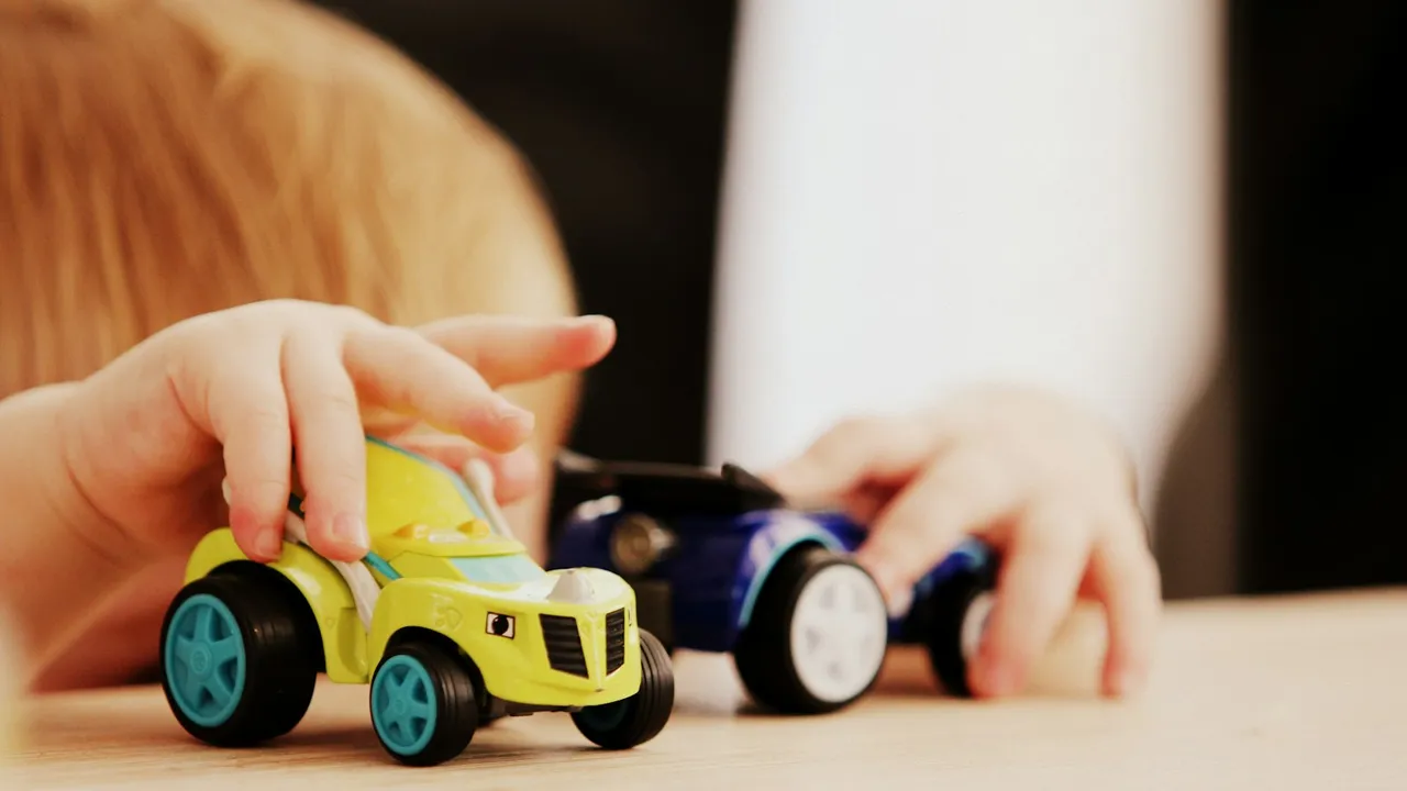 Niño pequeño jugando con autos de juguete sobre una mesa de madera