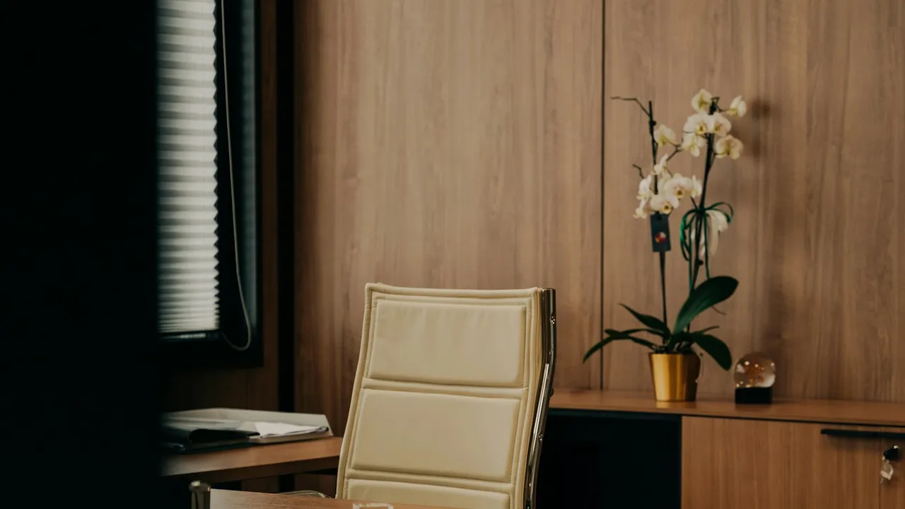 Escritorio ordenado con una silla y un florero con flores junto a la ventana