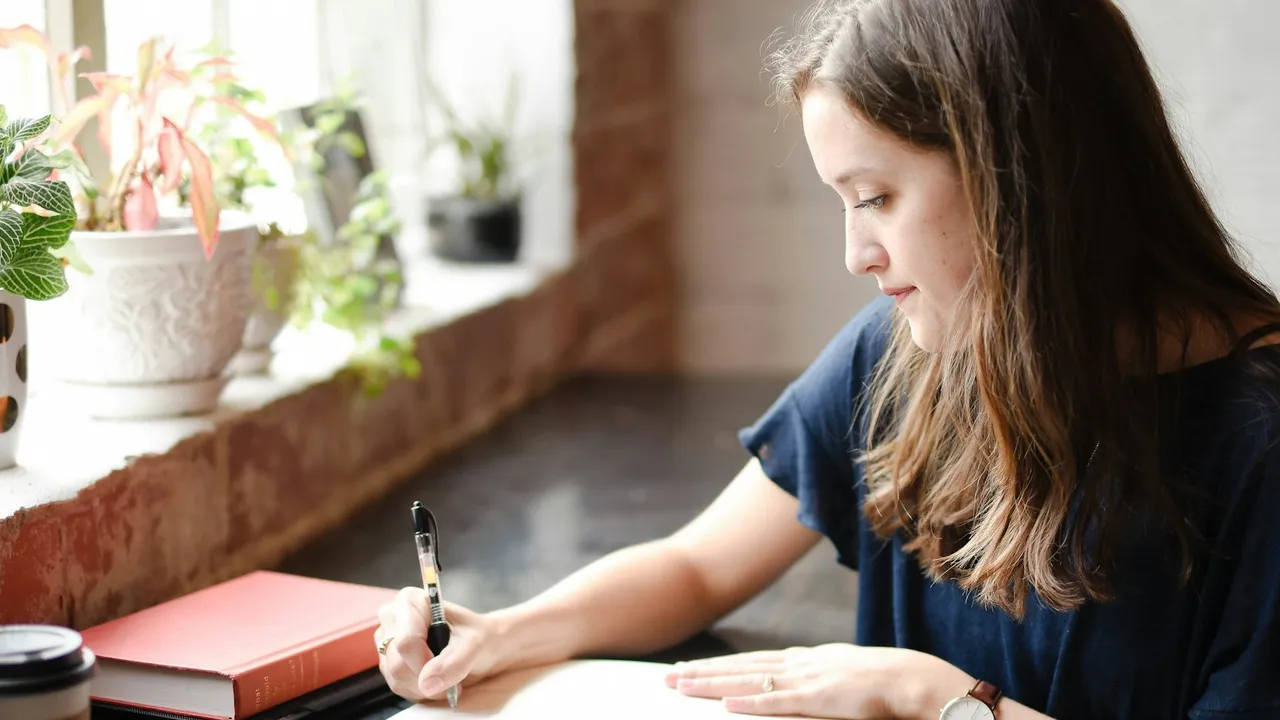 Persona escribiendo en un cuaderno junto a una ventana con luz natural